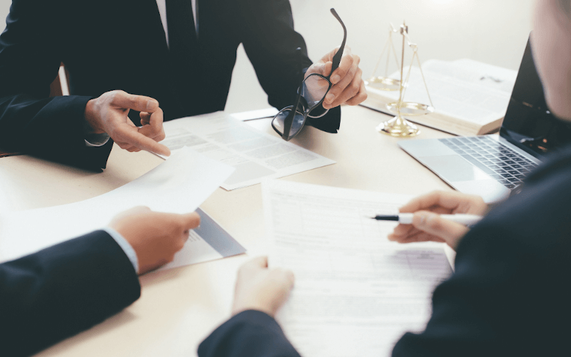 3 Personen sitzen mit einem Laptop und Schriftstücken am Tisch und diskutieren über ein Thema